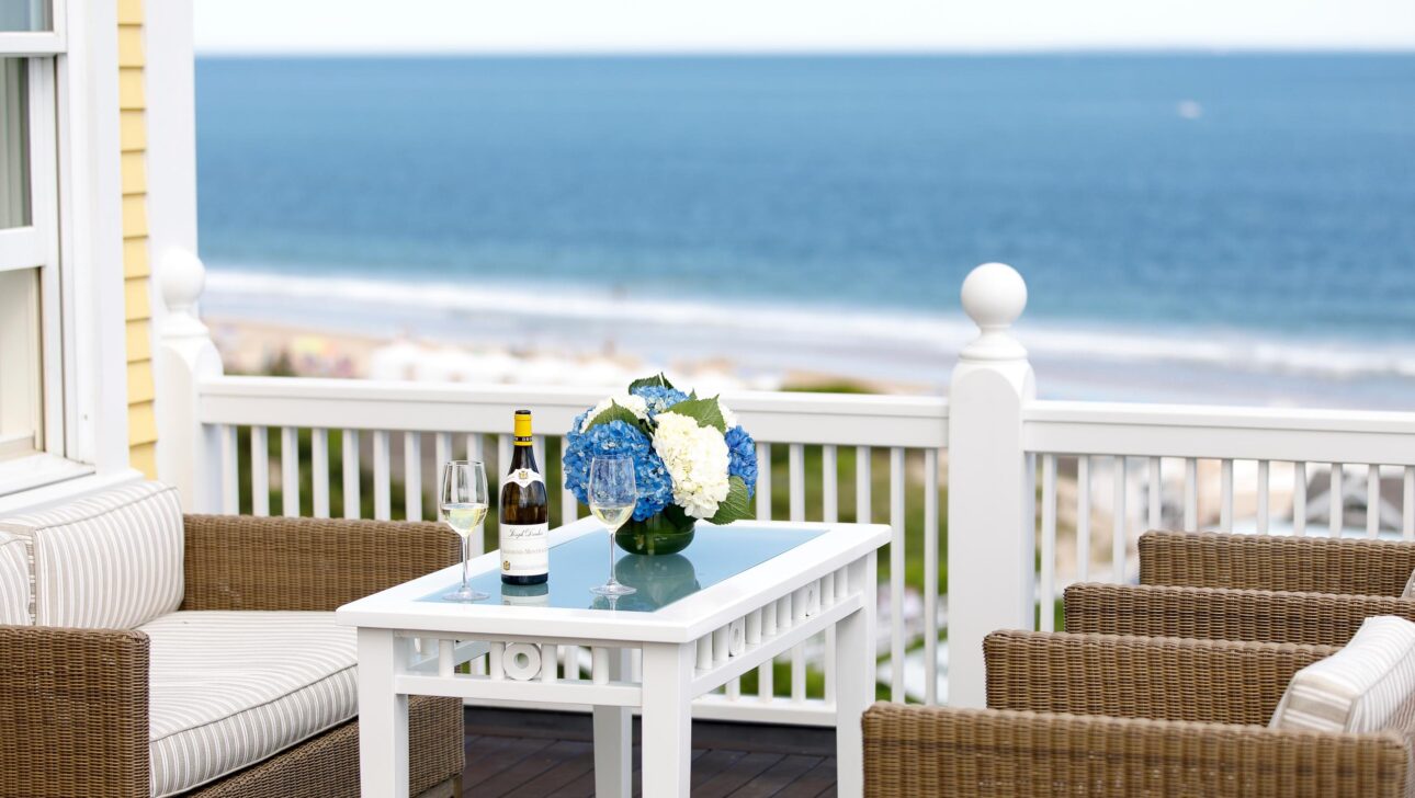 A veranda with seats and a table, overlooking an ocean.