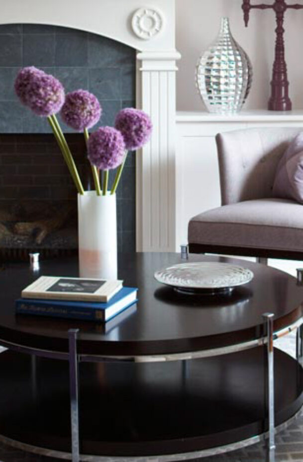 A round coffee table with a vase of purple flowers.