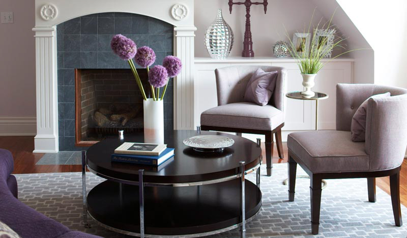 A round coffee table with a vase of purple flowers.