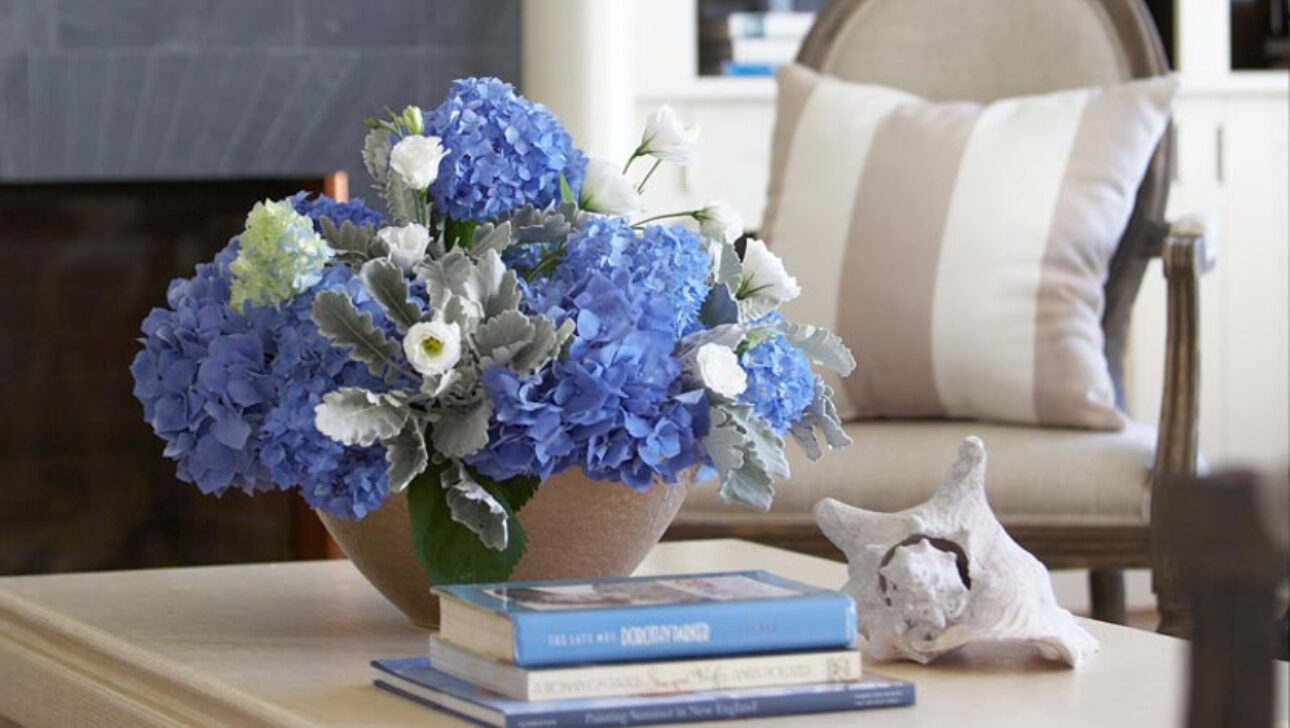 A vase of blue flowers and a stack of books on a coffee table.