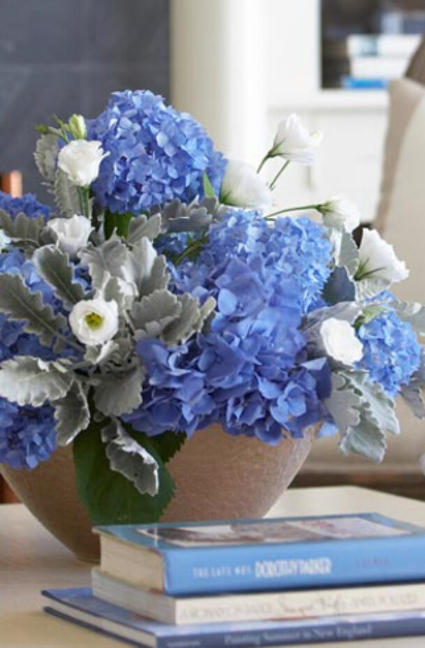 A vase of blue flowers and a stack of books on a coffee table.