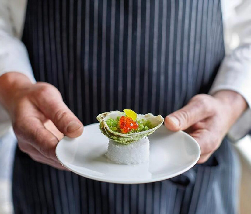 A chef holding a dish at COAST restaurant.