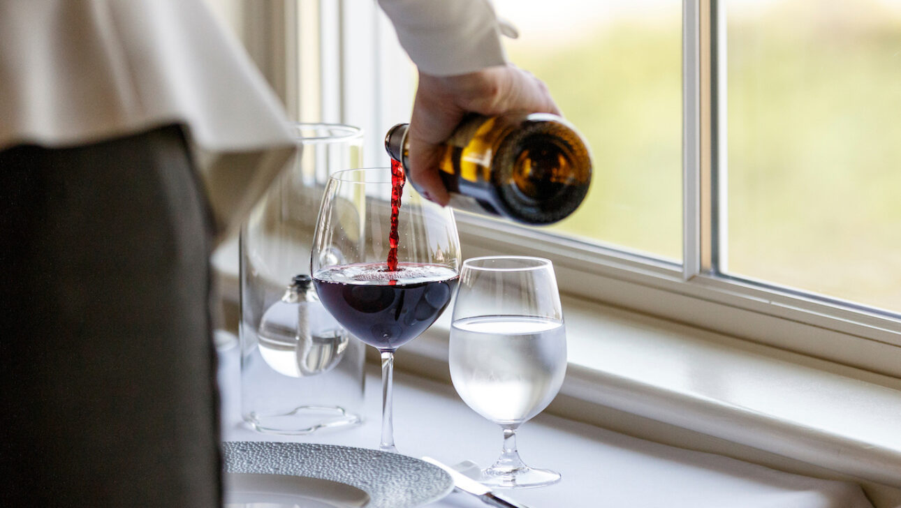 A server pouring a glass of red wine.