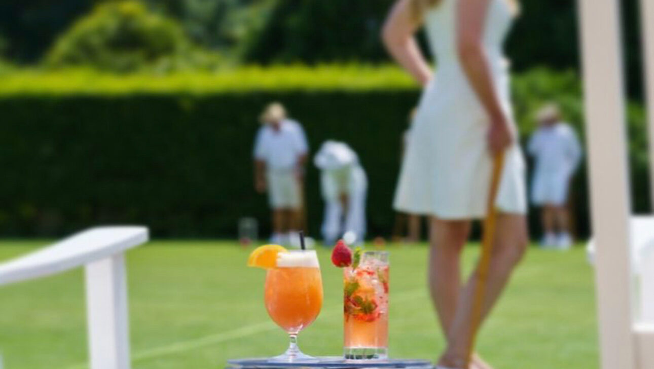 Drinks on a small table with people playing croquet in the background.