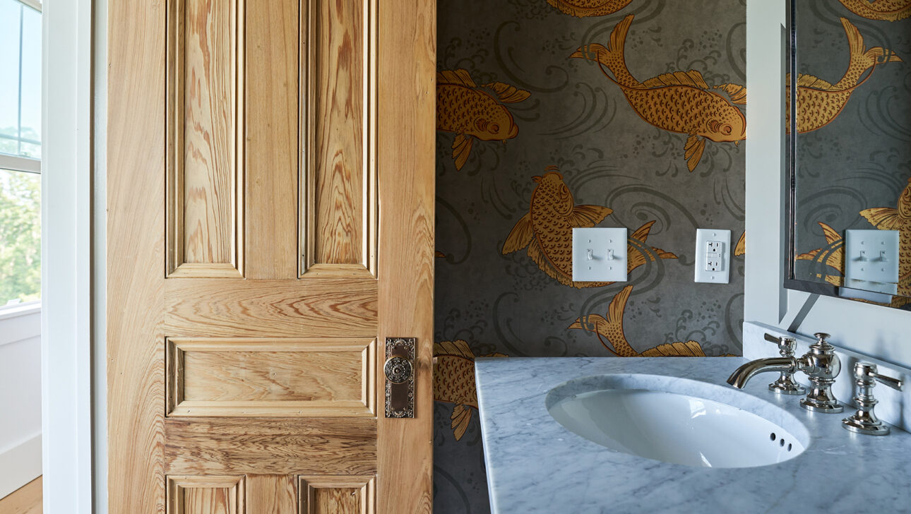 Bathroom with open wooden door, fish-patterned wallpaper, marble countertop, and silver faucet.