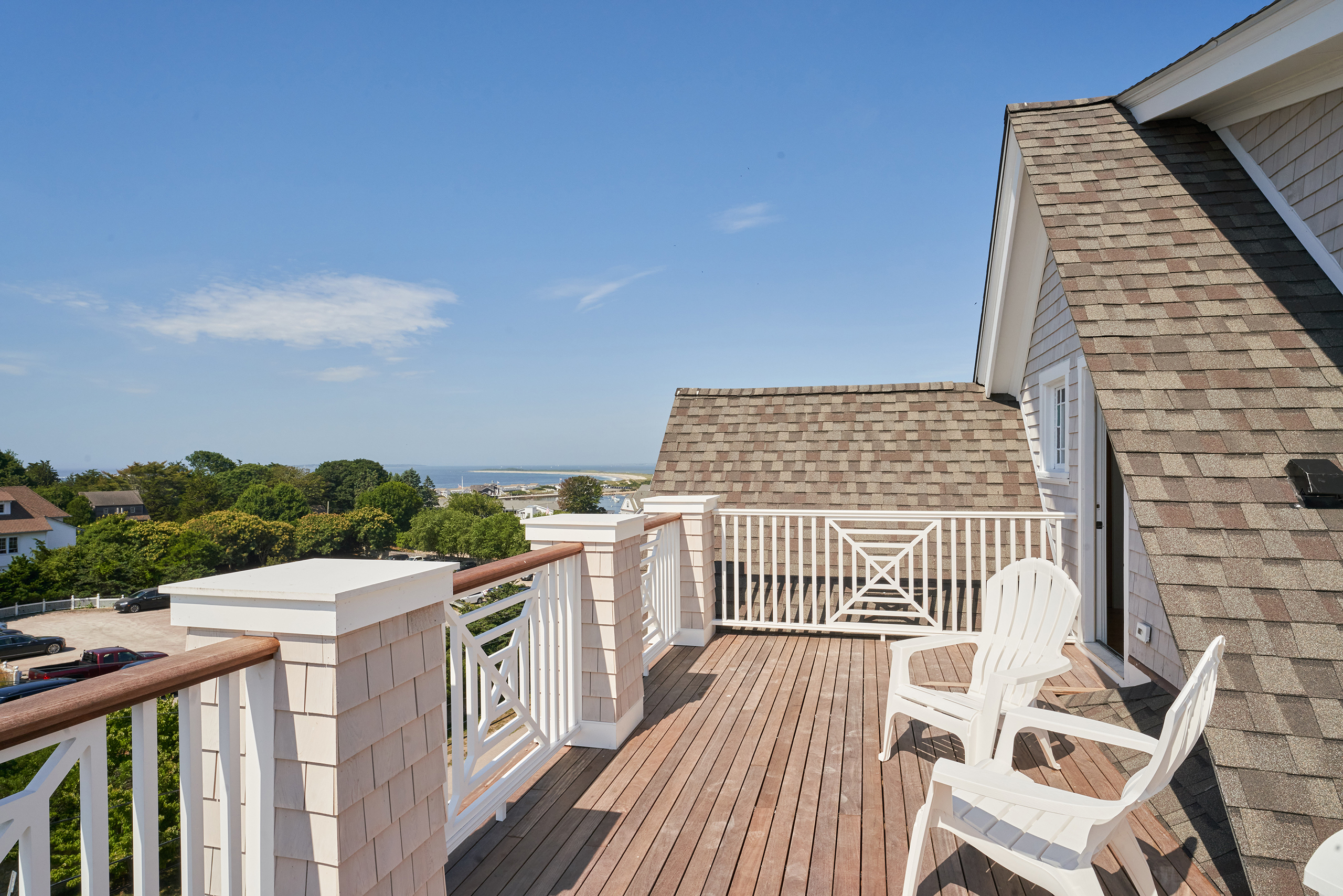 A rooftop deck with two white chairs overlooks a scenic view of trees and distant water under a clear blue sky.