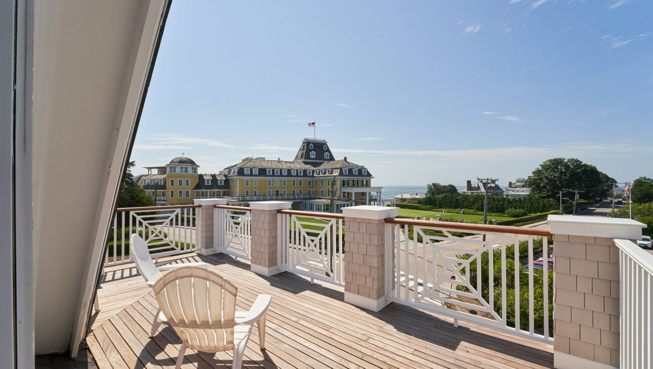 Balcony with two chairs overlooking a large yellow building and a distant ocean under a clear blue sky.