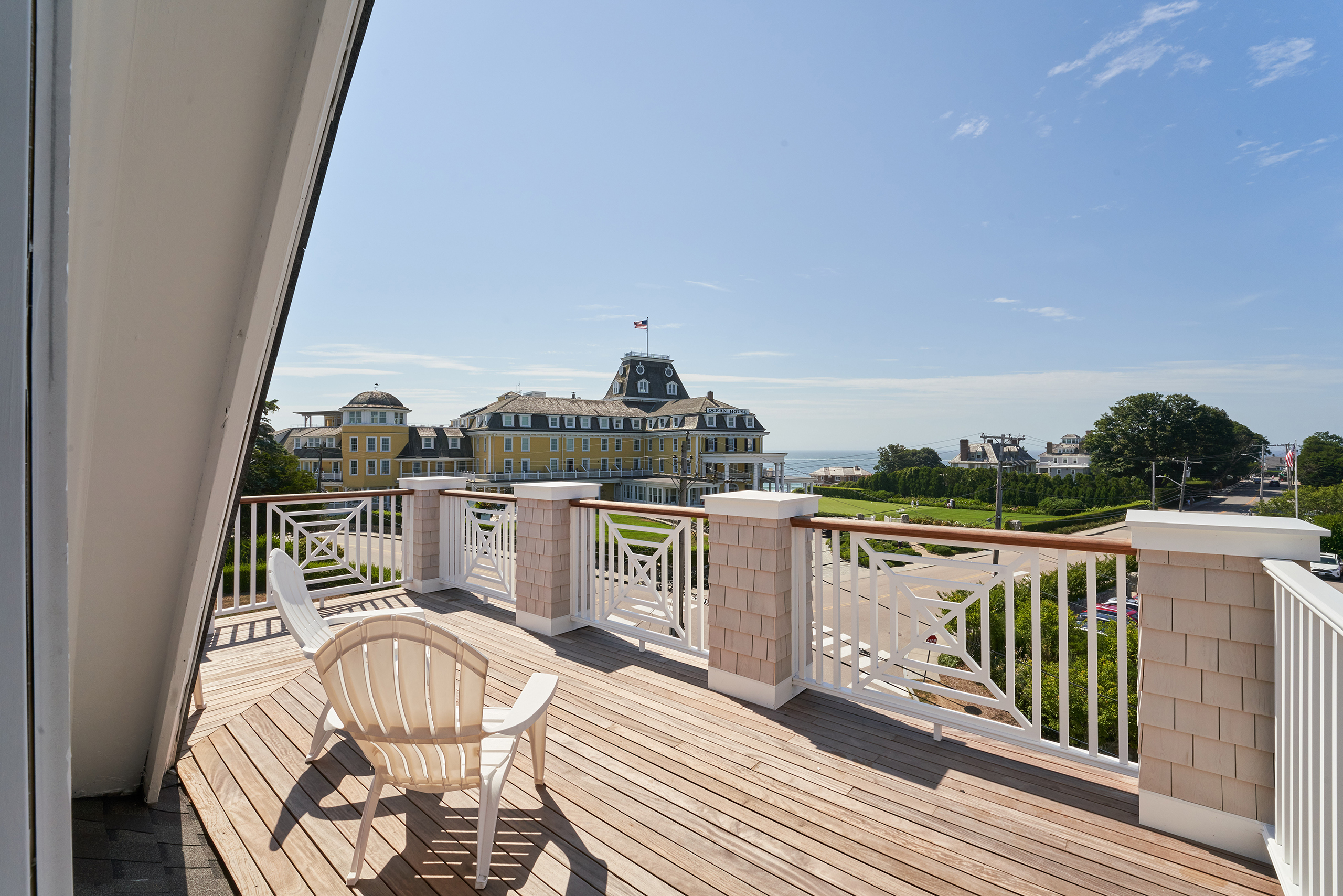 Balcony with two chairs overlooking a large yellow building and a distant ocean under a clear blue sky.