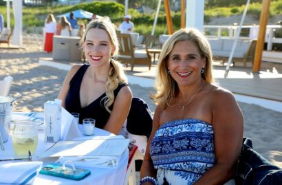 Two women sitting at an outdoor table on a sandy beach.
