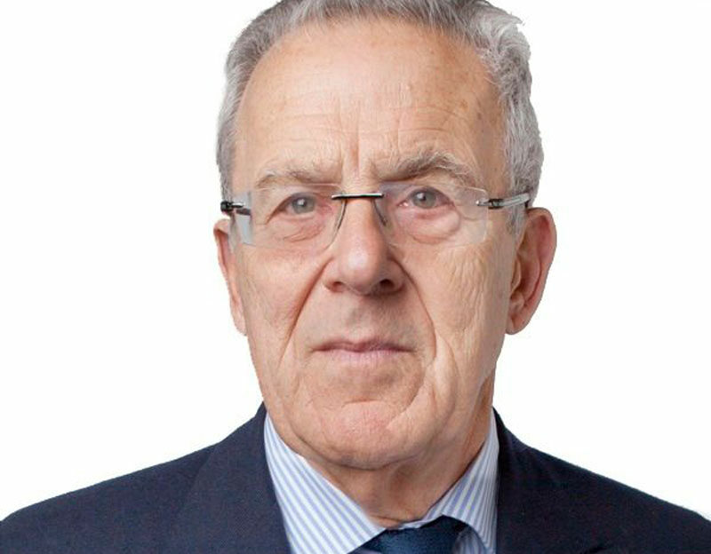 An older man wearing glasses and a suit, set against a plain white background.