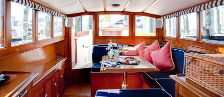 A cozy boat cabin with wood paneling, blue cushioned seating, and a table set with flowers and refreshments.