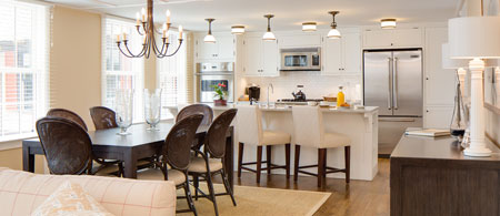 A modern kitchen and dining area with a dark wood table, eight chairs, white cabinetry, stainless steel appliances, and a chandelier.