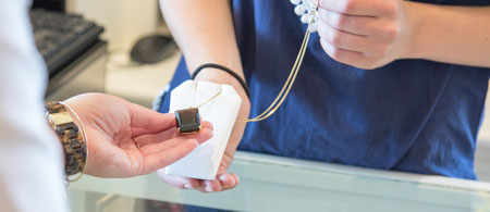 Two people exchanging a necklace over a counter, one holding a jewelry box.