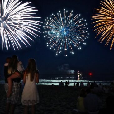 People on a beach watching colorful fireworks in the night sky.
